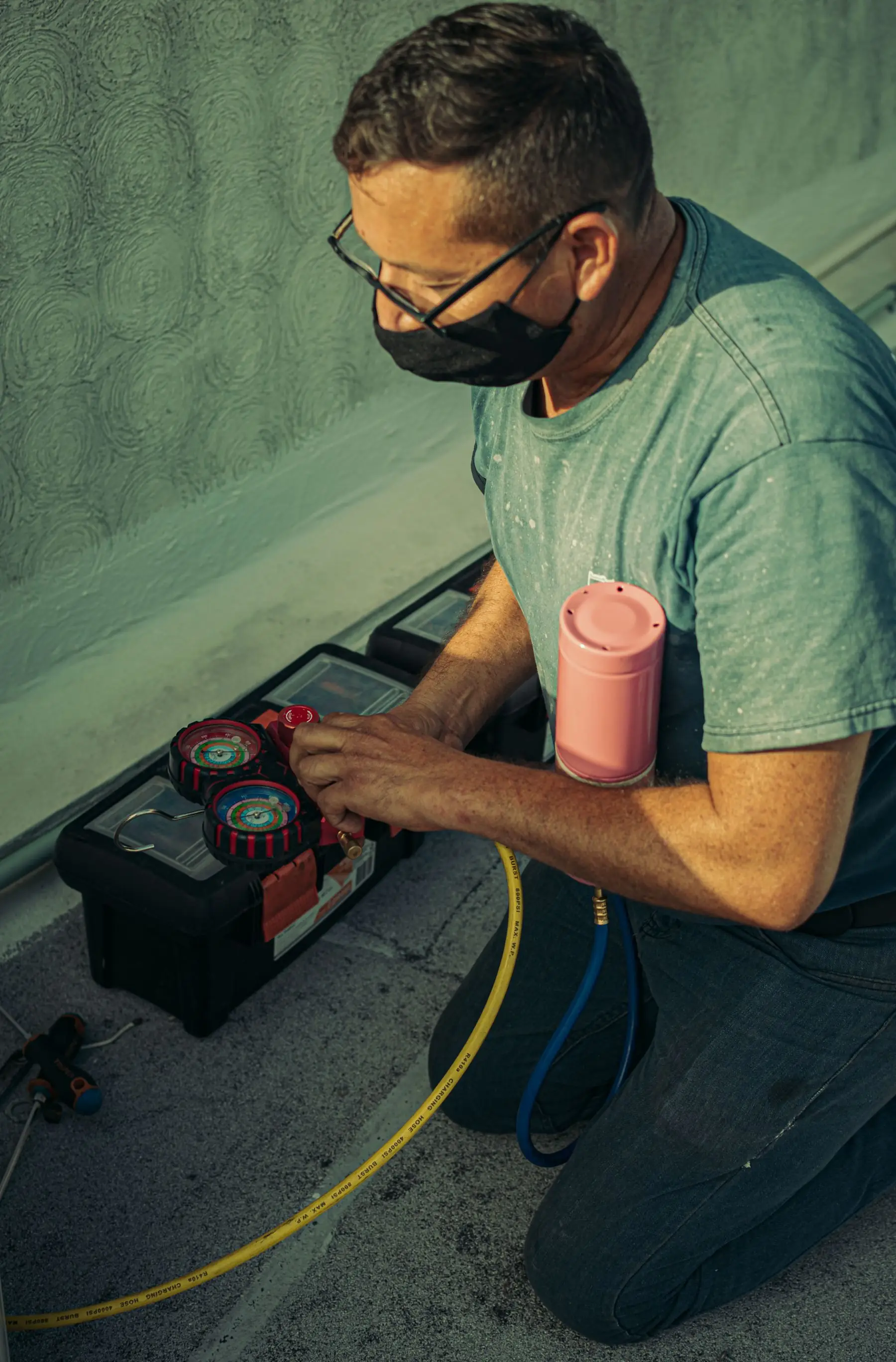 A technician kneeling to read manifold gauges while servicing an air conditioner