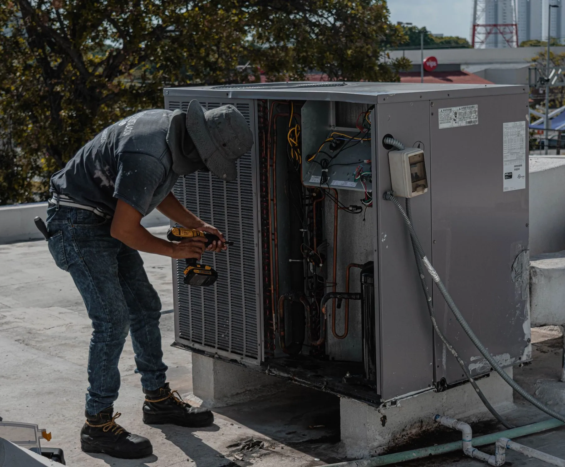 A technician in a bucket hat servicing a rooftop air conditioning unit