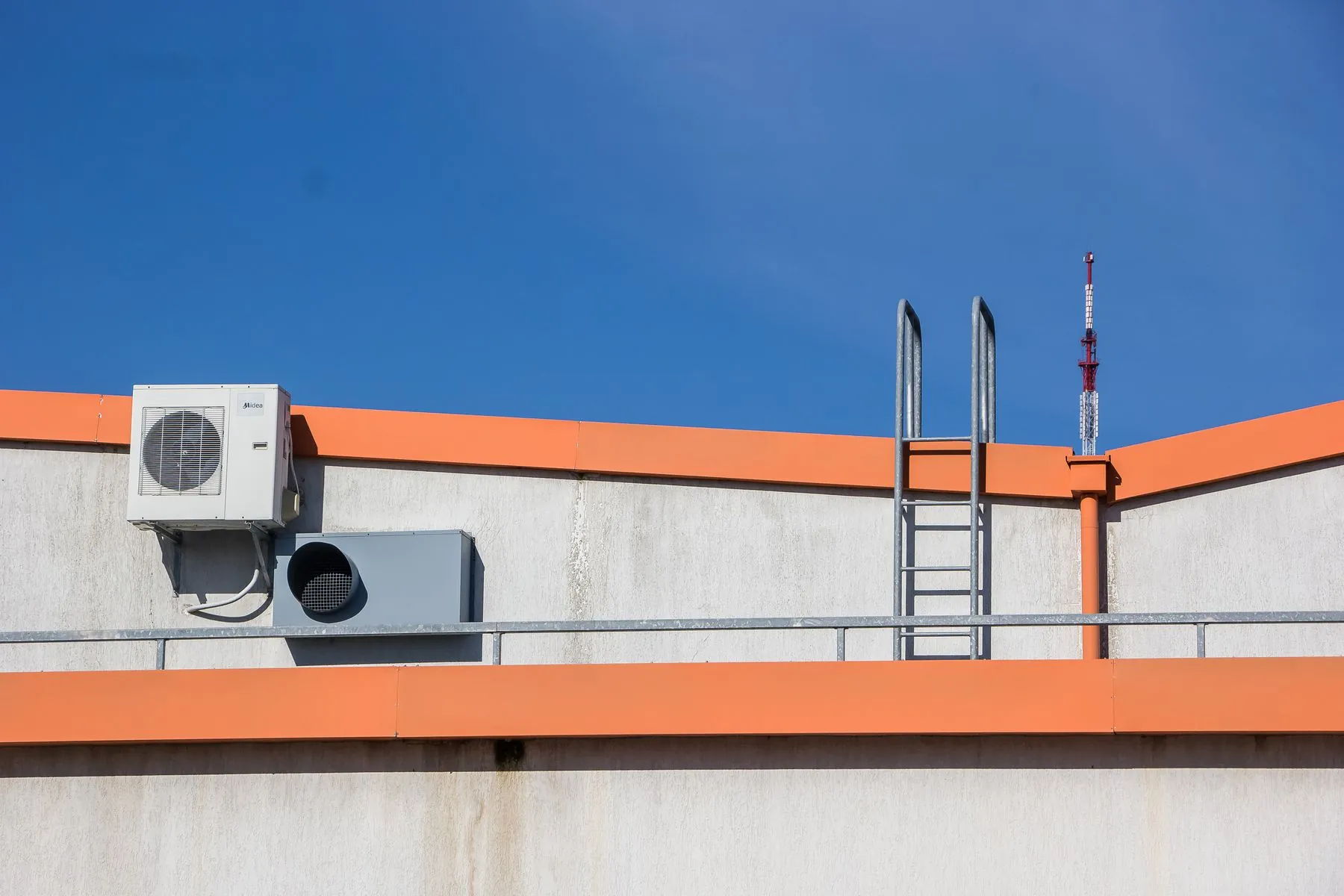 An outdoor air conditioning unit on a rooftop with an orange parapet under a blue sky