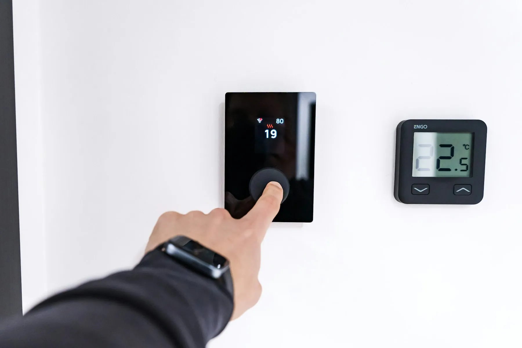 A hand turning a modern digital wall thermostat beside a small display